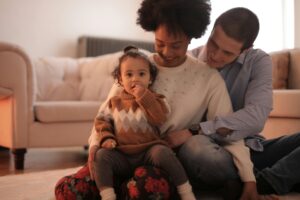 Husband, wife, and toddler sitting on the floor of a living room