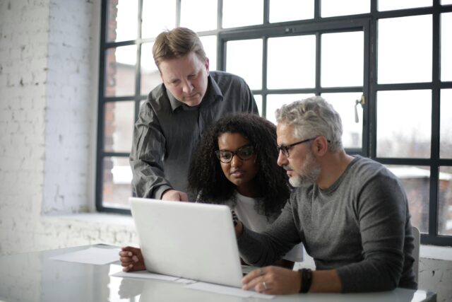 Three people sitting around a desk looking at the same computer